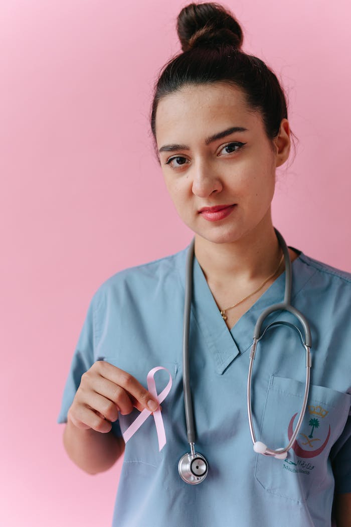 Female doctor in scrubs with pink ribbon for breast cancer awareness.